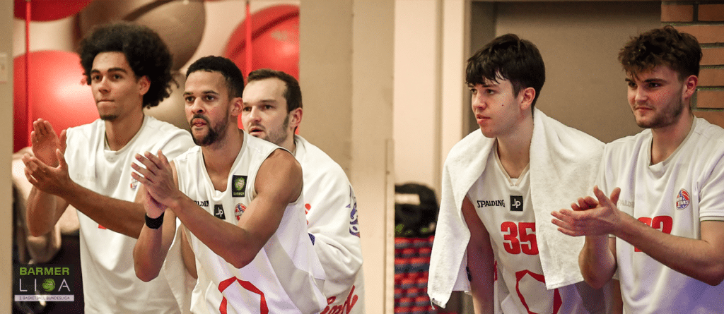 Fünf Basketballspieler der RheinStars Köln in weißen Trikots klatschen zusammen.