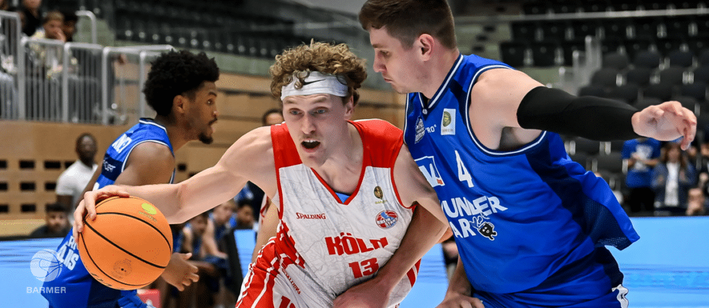 Basketballspiel: RheinStars-Köln-Spieler in Rot dribbbelt gegen zwei Gegner in Blau.