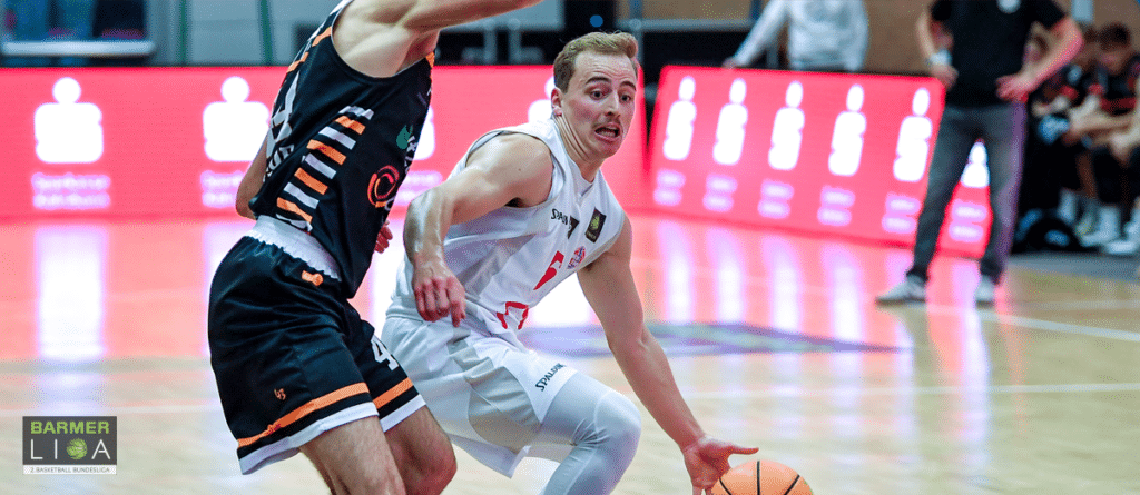Basketballspieler der RheinStars Köln dribbelt gegen Gegner in schwarzem Trikot.
