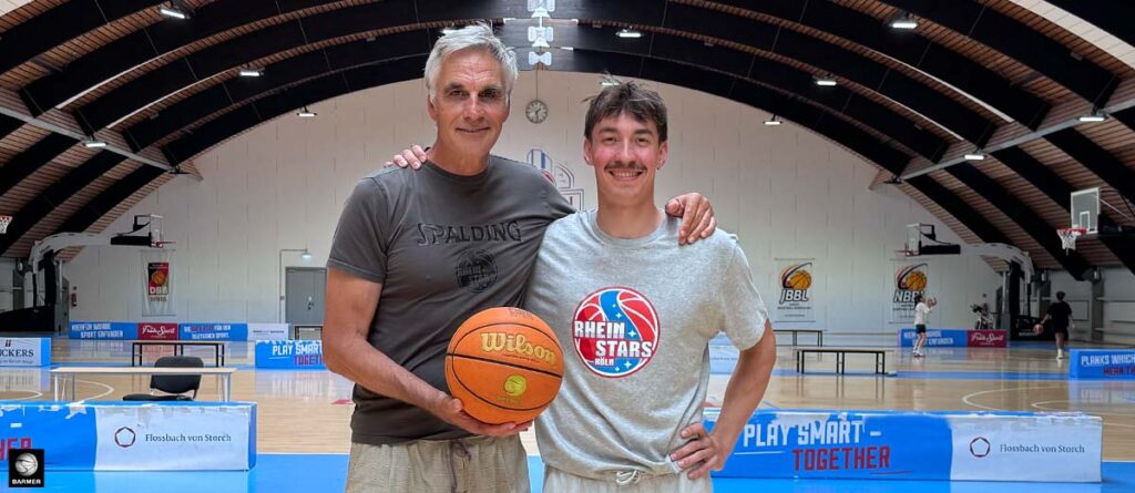 Zwei Männer posieren mit Basketball in einer RheinStars-Köln-Sporthalle.