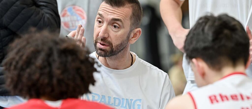 Ein Trainer der RheinStars Köln gibt Anweisungen an Spieler in roten Trikots.