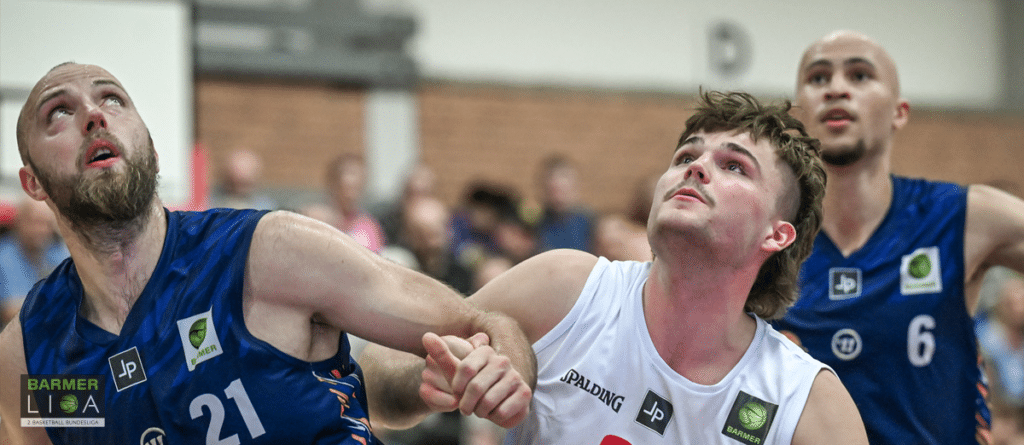 Basketballspiel der RheinStars Köln: Spieler in weißem und blauem Trikot kämpfen um den Ball unter dem Korb.