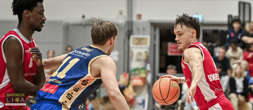 Basketballspiel der RheinStars Köln: Spieler in roten Trikots gegen Gegner in blau-goldenem Trikot.