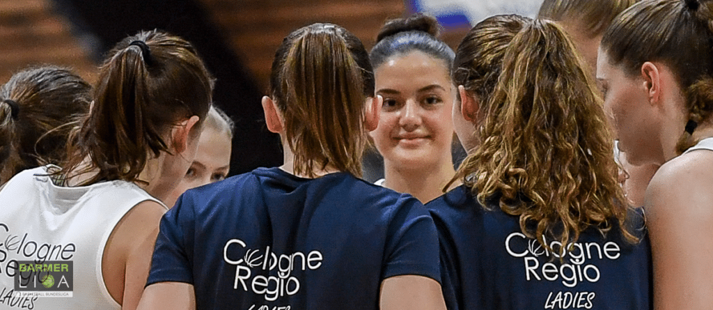 Basketballteam der RheinStars Köln in dunkelblauen Trainingstrikots beim Teamgespräch.