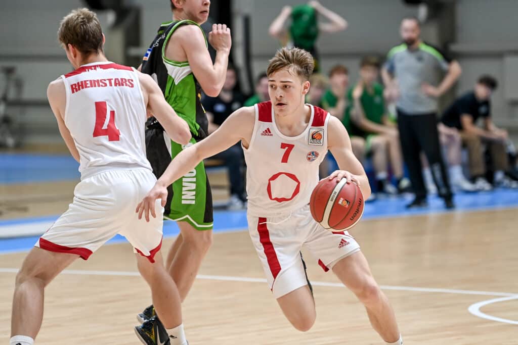 RheinStars-Spieler Nummer 7 dribbelt mit Basketball während Nummer 4 Deckung spielt.