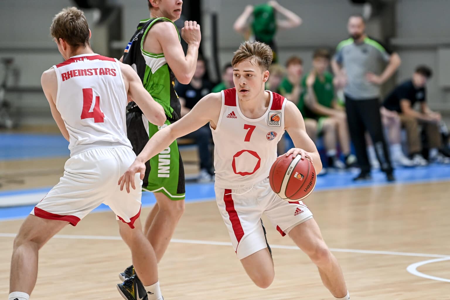 RheinStars-Spieler Nummer 7 dribbelt mit Basketball während Nummer 4 Deckung spielt.