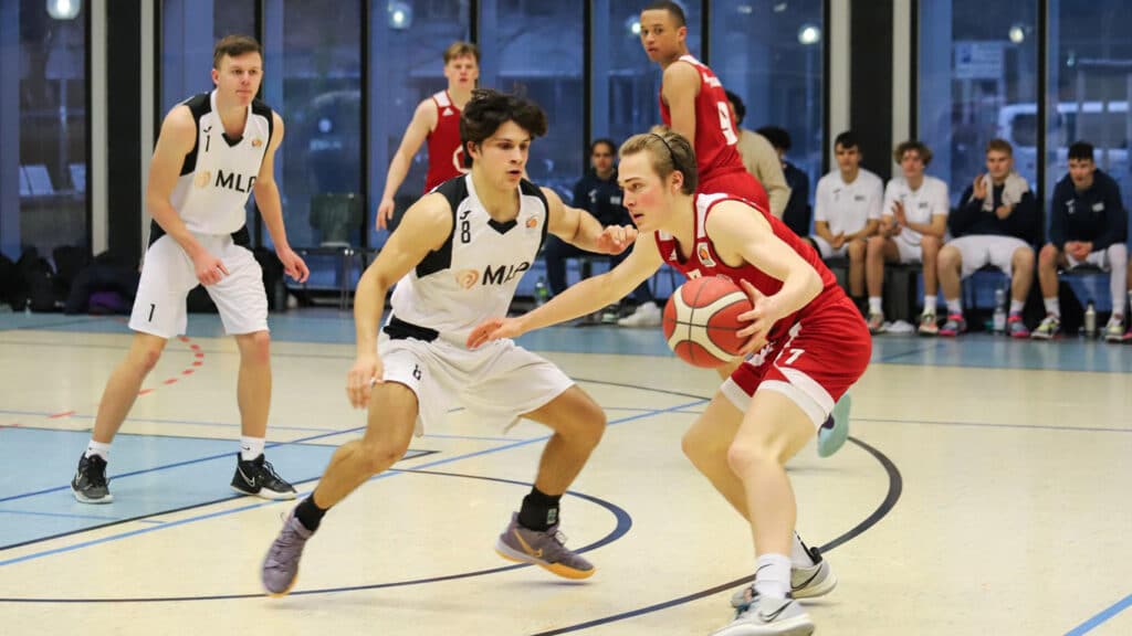Basketballspiel der RheinStars Köln: Spielerin im roten Trikot dribbelt, weiße Defensivspielerin versucht zu blocken.