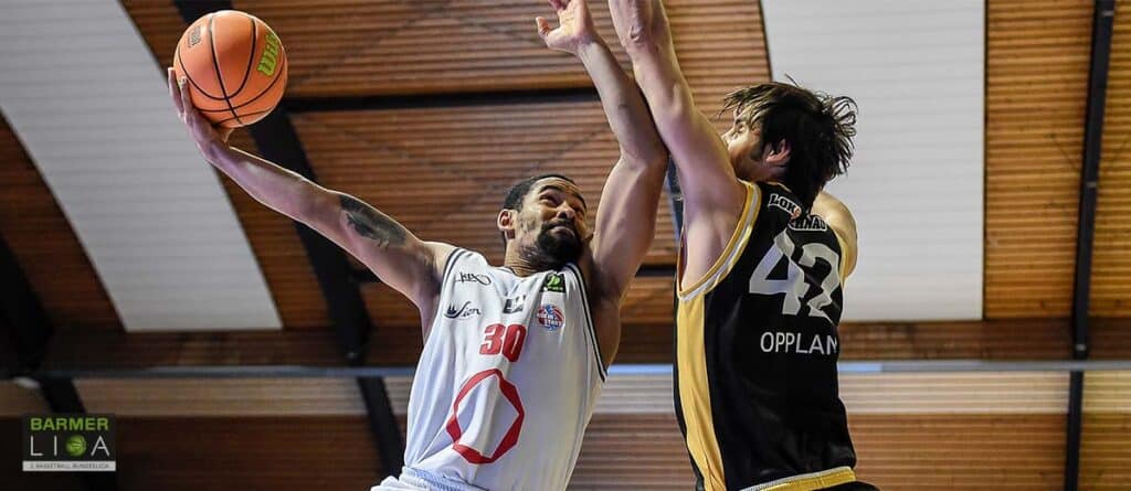 Basketballspieler der RheinStars Köln wirft Ball unter Druck eines Gegenspielers.