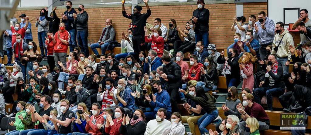 Zuschauer der RheinStars Köln applaudieren in einer Sporthalle während eines Spiels.