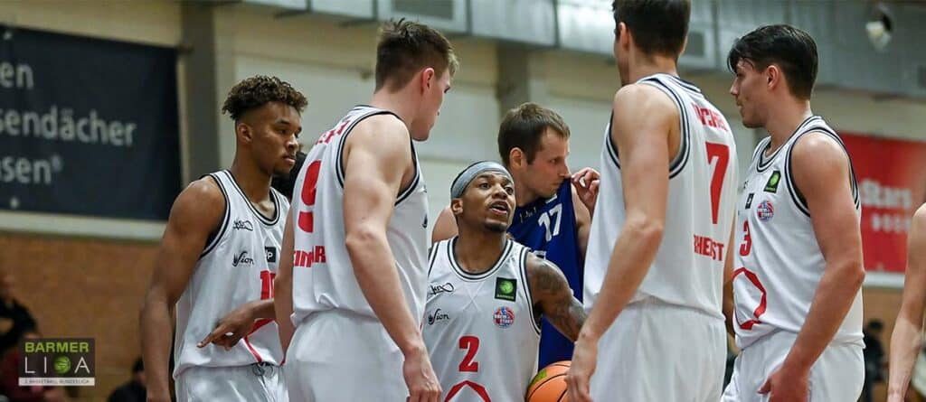RheinStars Köln Basketballteam in weißen Trikots beim Teamgespräch in der Halle.