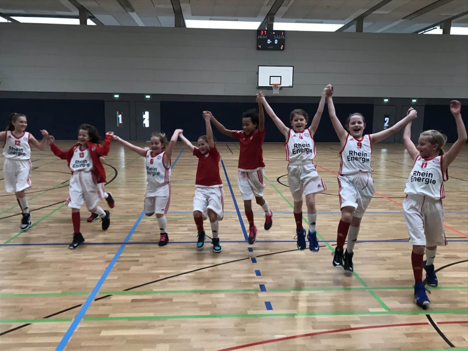Junge Basketballspielerinnen der RheinStars Köln springen jubelnd in einer Sporthalle.