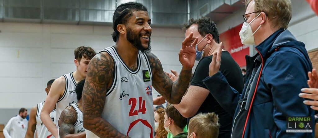 Basketballspieler der RheinStars Köln mit Nummer 24 lacht mit Trainern und Zuschauern.