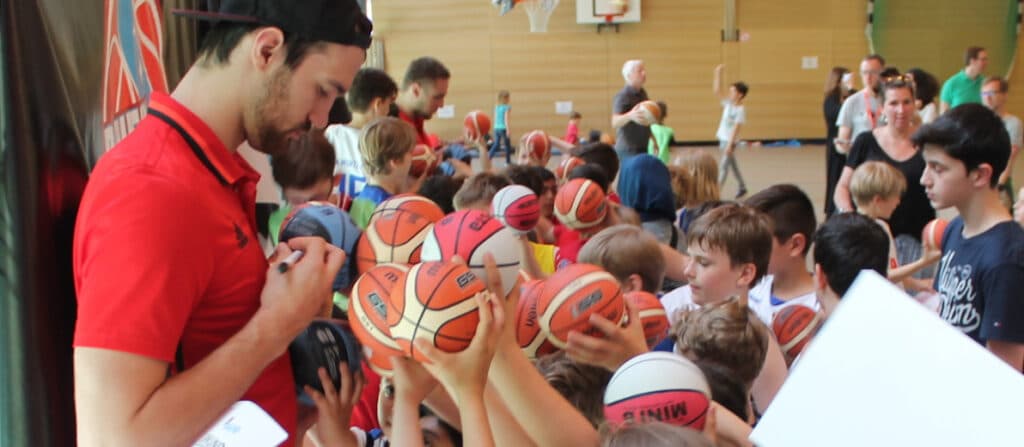 Ein Trainer der RheinStars Köln unterrichtet Kinder im Basketballtraining in einer Sporthalle.
