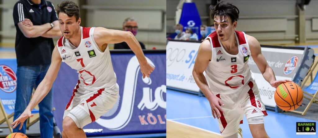 Zwei Spieler der RheinStars Köln in weißen Trikots mit roten Details beim Basketball spielen.