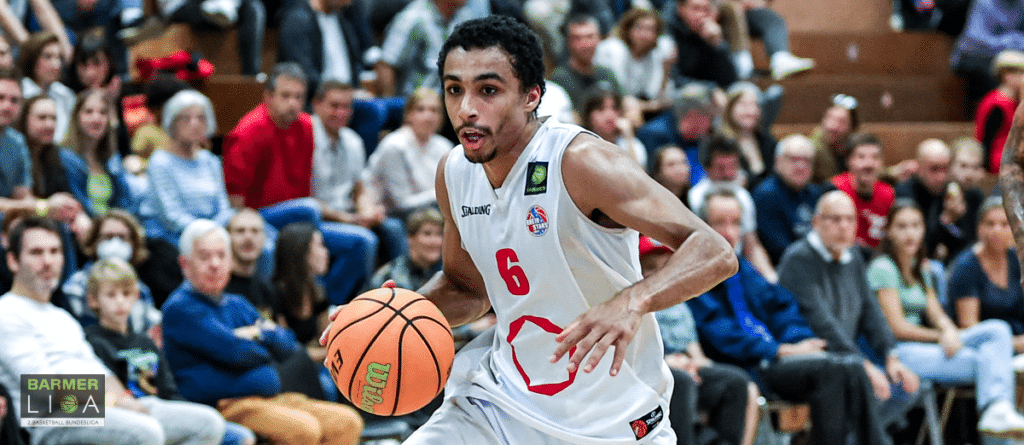 Basketballspieler der RheinStars Köln mit Nummer 6 dribbelt Ball während Spiel vor Zuschauern.