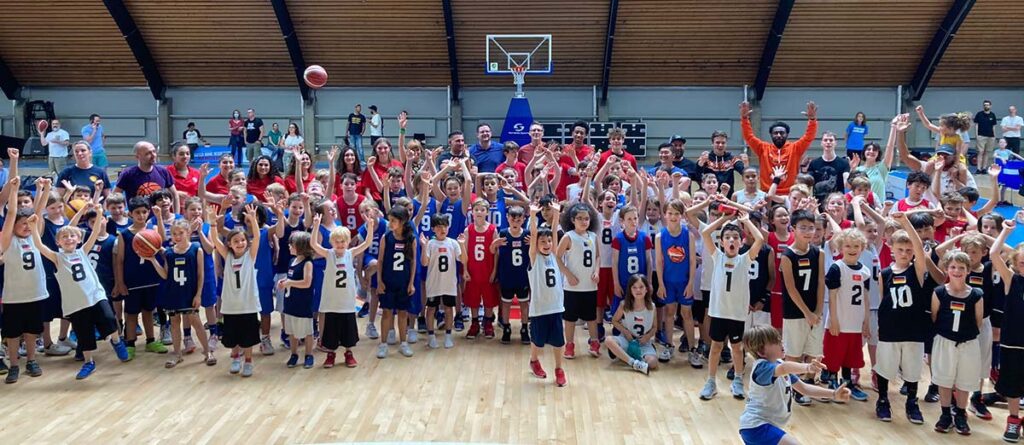 Große Gruppe von Basketballspielern der RheinStars Köln in einer Sporthalle, posierend mit erhobenen Armen.