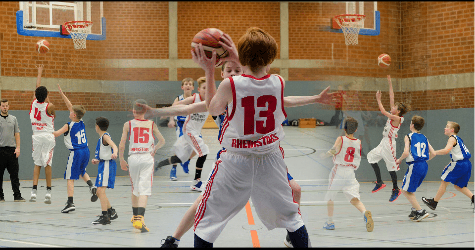 Jugendbasketballspiel der RheinStars Köln in einer Sporthalle mit Spielern in roten und blauen Trikots.