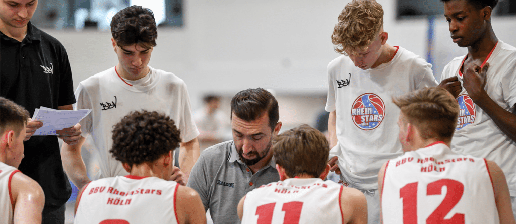 Basketballtrainer bespricht sich mit jungen RheinStars-Spielern in der Halle.