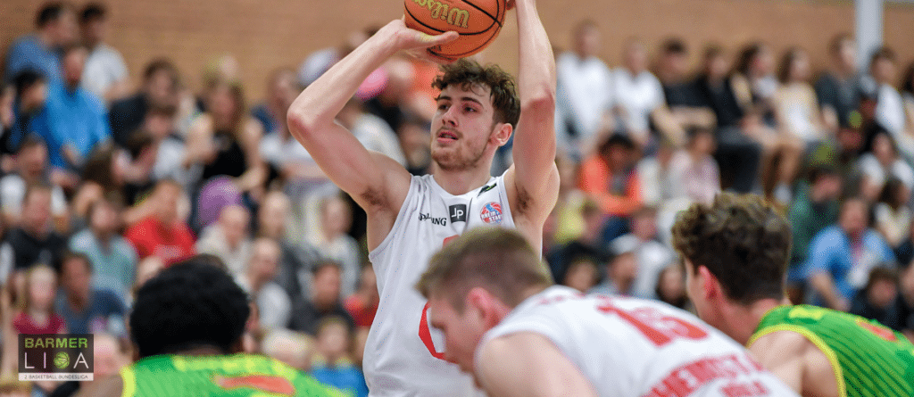 Basketballspieler der RheinStars Köln wirft Ball während Heimspiel vor Zuschauern.