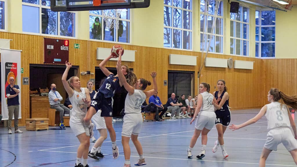 Volleyballspiel der RheinStars Köln in Sporthalle: Spielerin in Dunkelblau springt zum Angriffsschlag, Gegnerinnen in Weiß in Abwehrposition.
