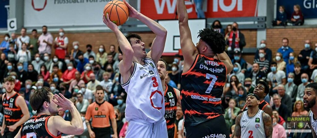 Basketballspiel: RheinStars-Spieler wirft Ball, Gegenspieler versucht zu blocken.